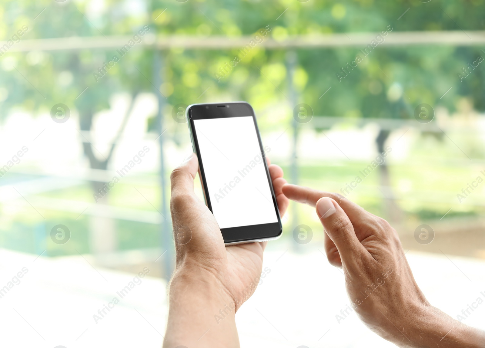 Photo of Young man holding mobile phone with blank screen on blurred background, closeup