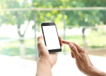 Young man holding mobile phone with blank screen on blurred background, closeup