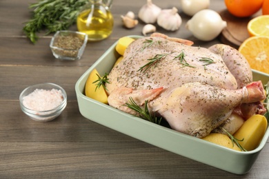 Photo of Raw chicken with potatoes and rosemary on wooden table