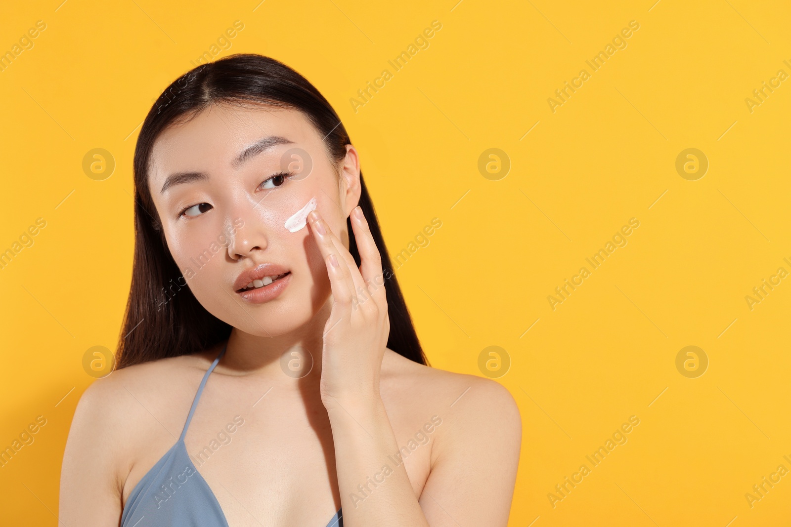 Photo of Beautiful young woman with sun protection cream on her face against orange background, space for text