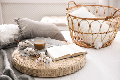 Composition with cup of drink, cotton and book on wicker pouf indoors