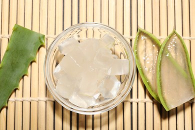 Photo of Aloe vera gel and slices of plant on bamboo mat, flat lay