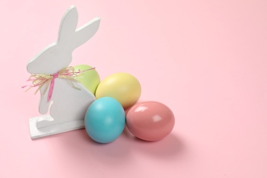 Cute wooden Easter bunny and dyed eggs on color background, space for text