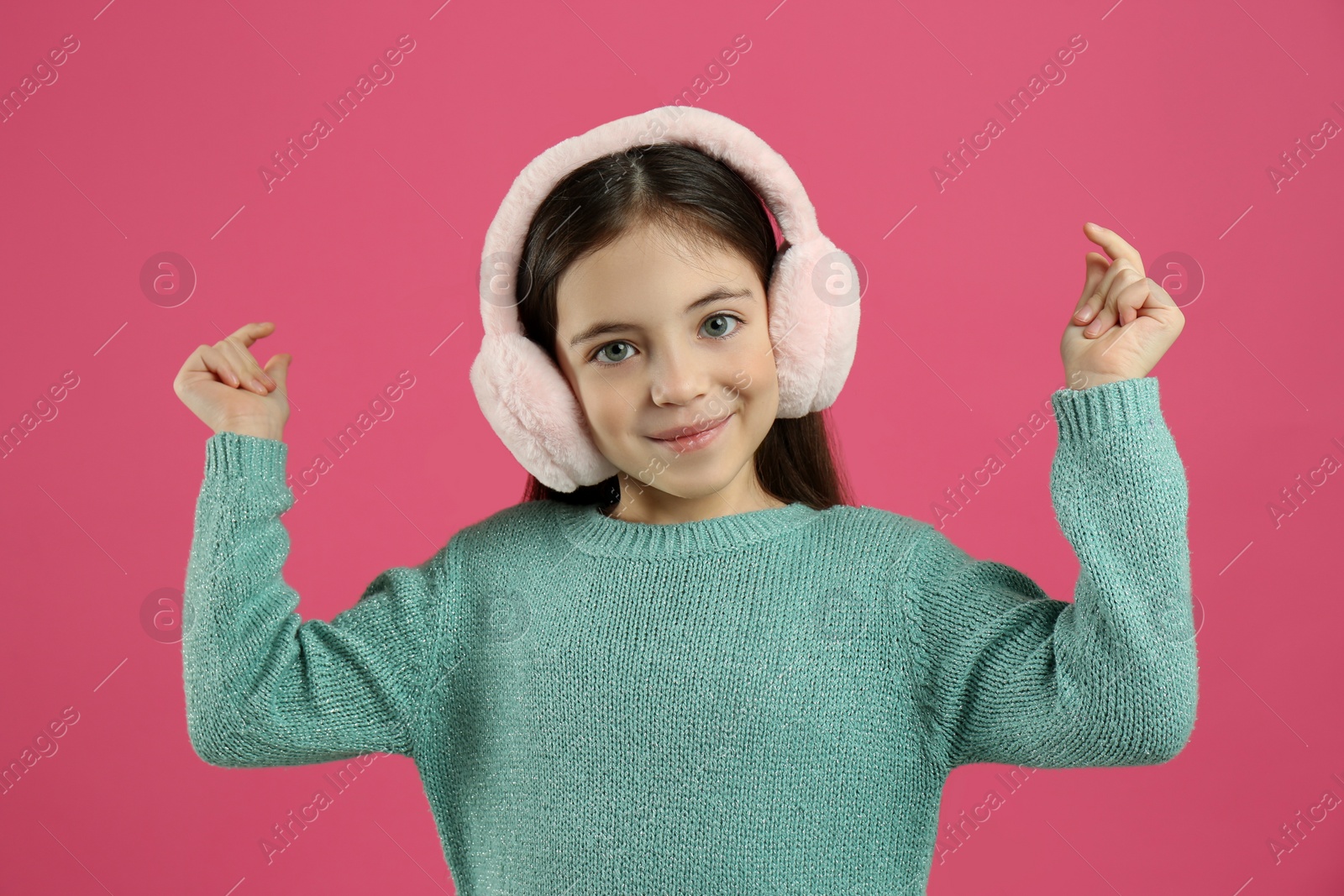 Photo of Cute little girl wearing stylish earmuffs on pink background