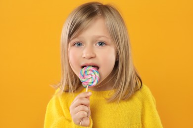 Portrait of happy girl licking lollipop on orange background