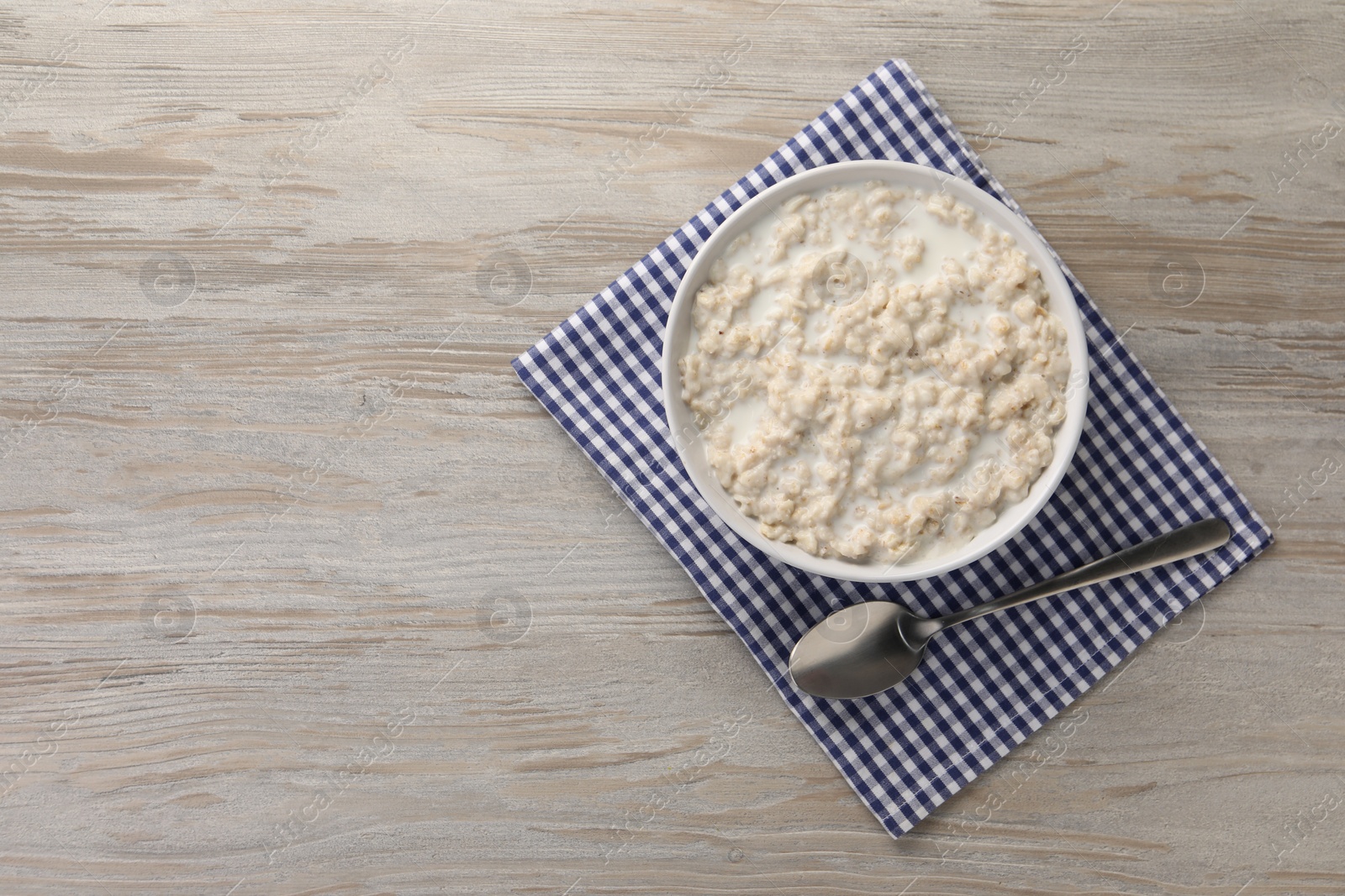 Photo of Tasty boiled oatmeal in bowl and spoon on wooden table, top view. Space for text