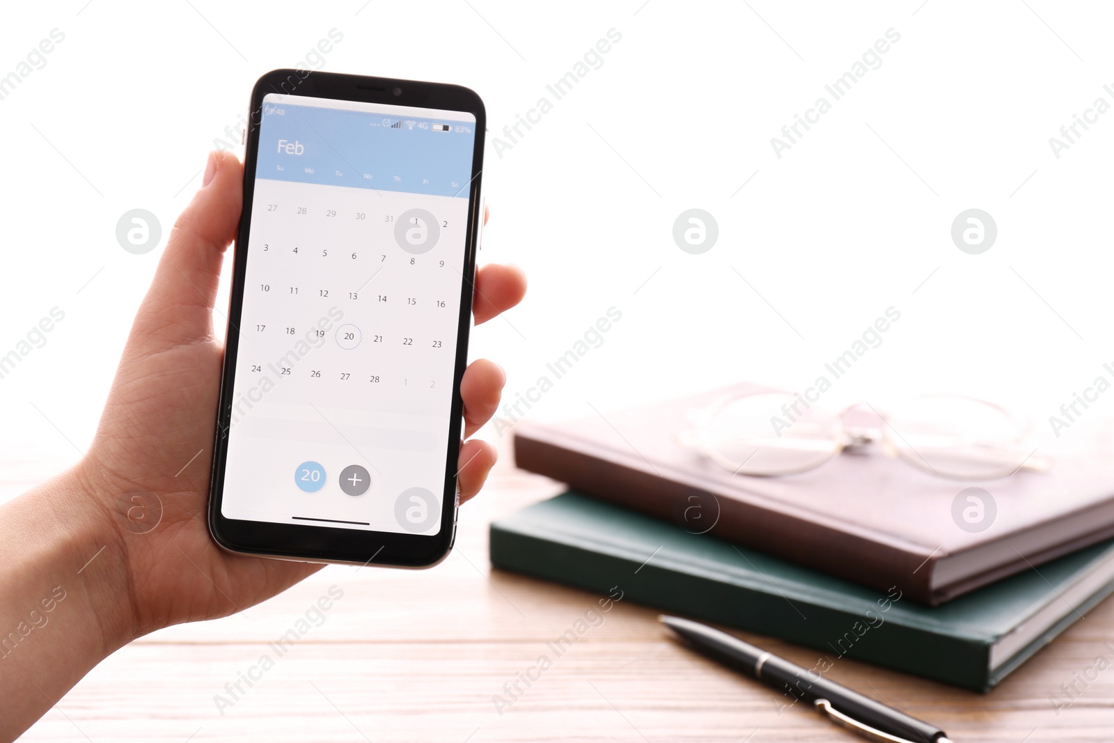 Photo of Woman holding smartphone with calendar app above table, closeup