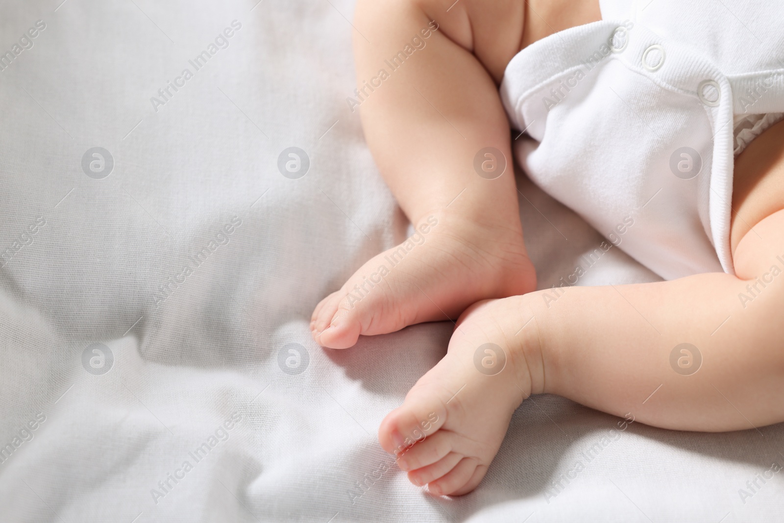Photo of Little baby in bodysuit on bed, closeup. Space for text