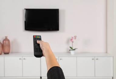 Photo of Woman switching channels on TV set with remote control at home
