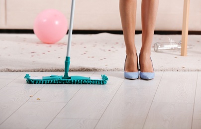 Photo of Woman with mop cleaning messy room after party, closeup view of legs