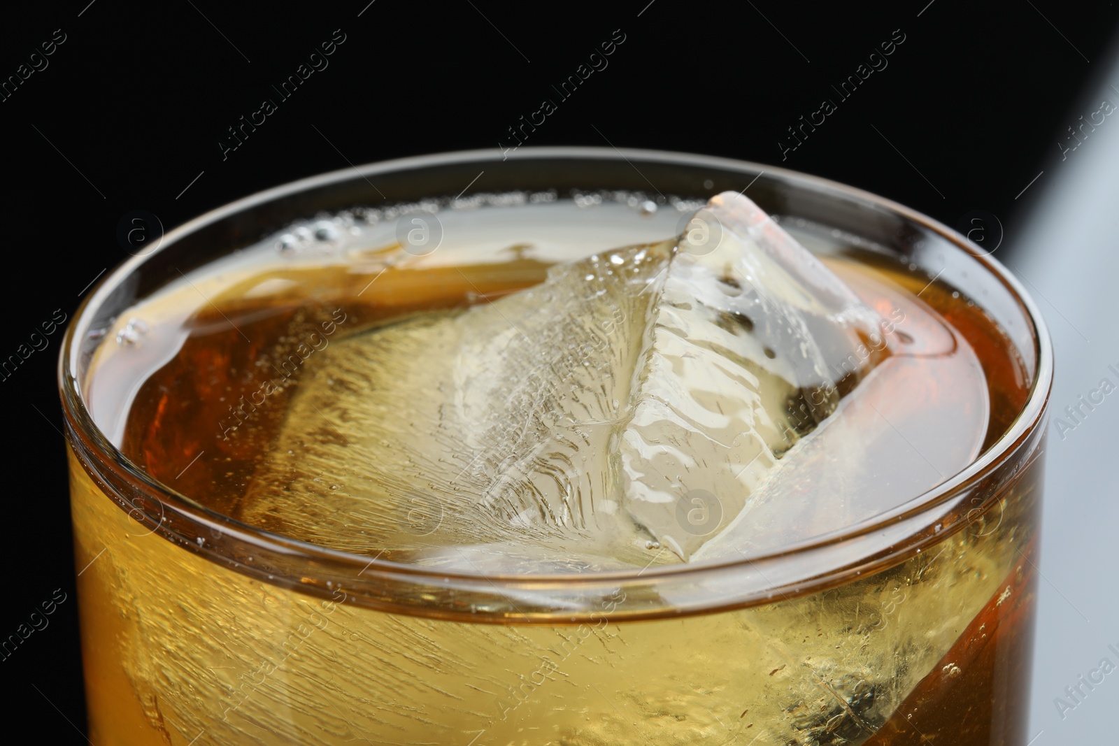 Photo of Tasty whiskey and ice in glass on black background, closeup