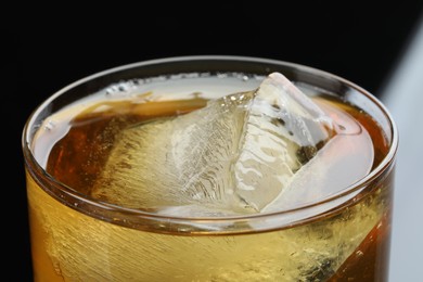 Photo of Tasty whiskey and ice in glass on black background, closeup