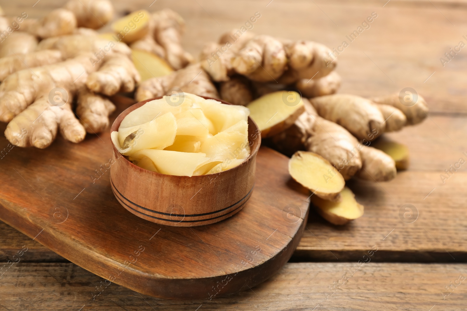 Photo of Spicy pickled ginger and root on wooden table, space for text