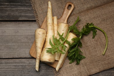 Photo of Many fresh ripe parsnips and green leaves on wooden table, flat lay