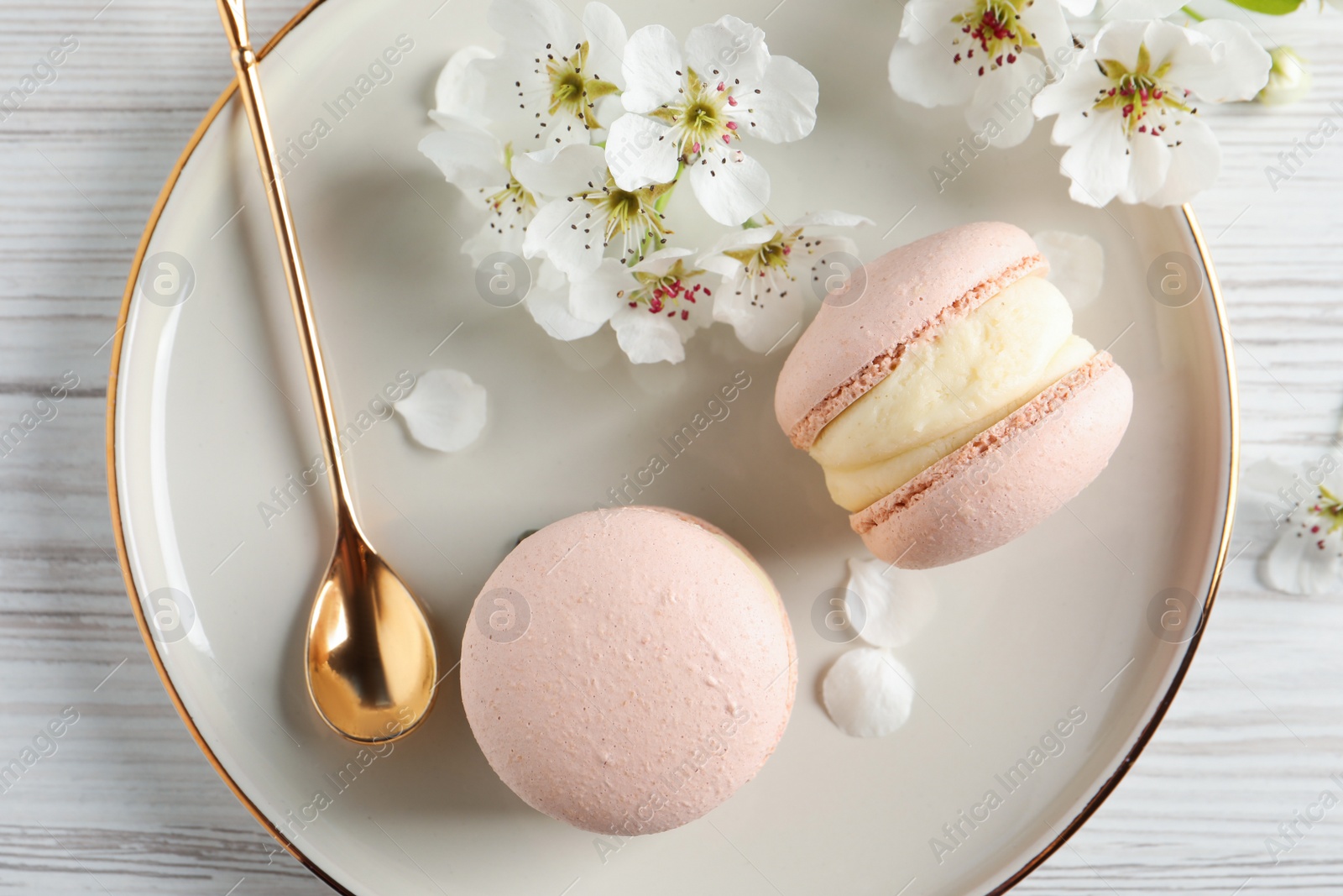 Photo of Delicious pink macarons and flowers on white wooden table, flat lay