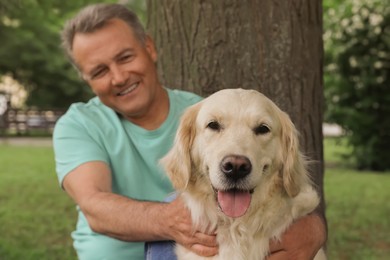 Photo of Happy senior man with his Golden Retriever dog resting under tree in park