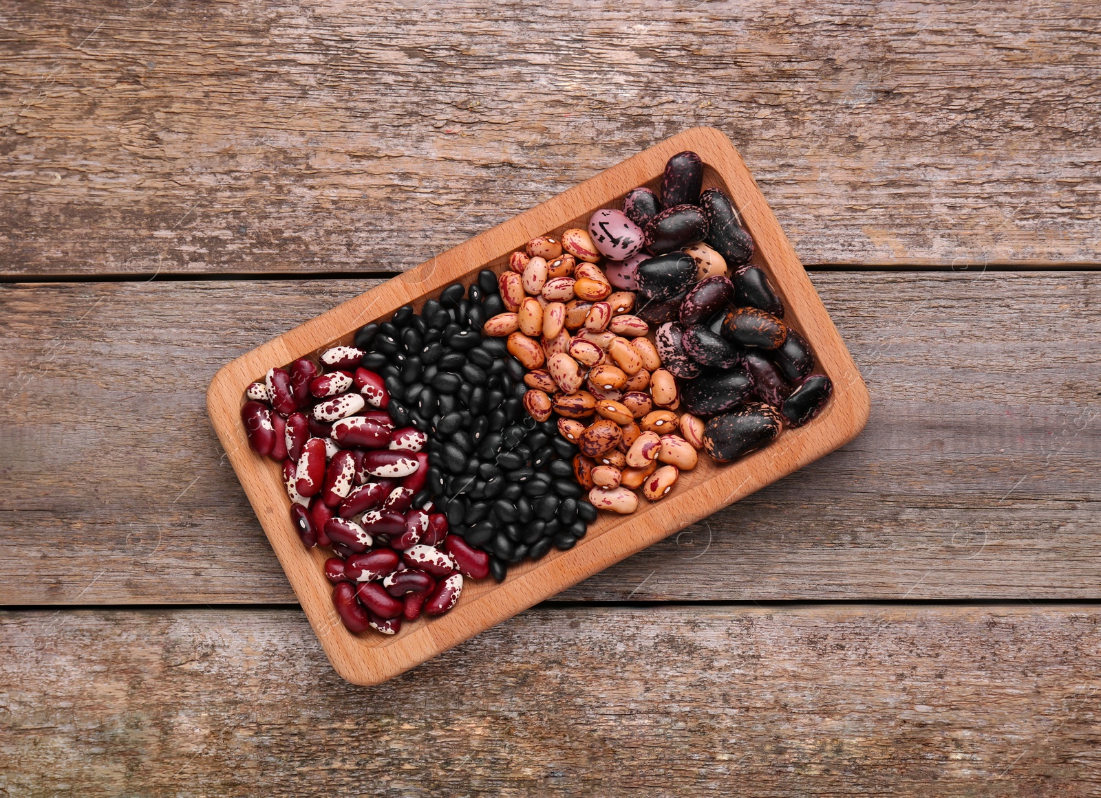 Photo of Plate with different kinds of dry kidney beans on wooden table, top view