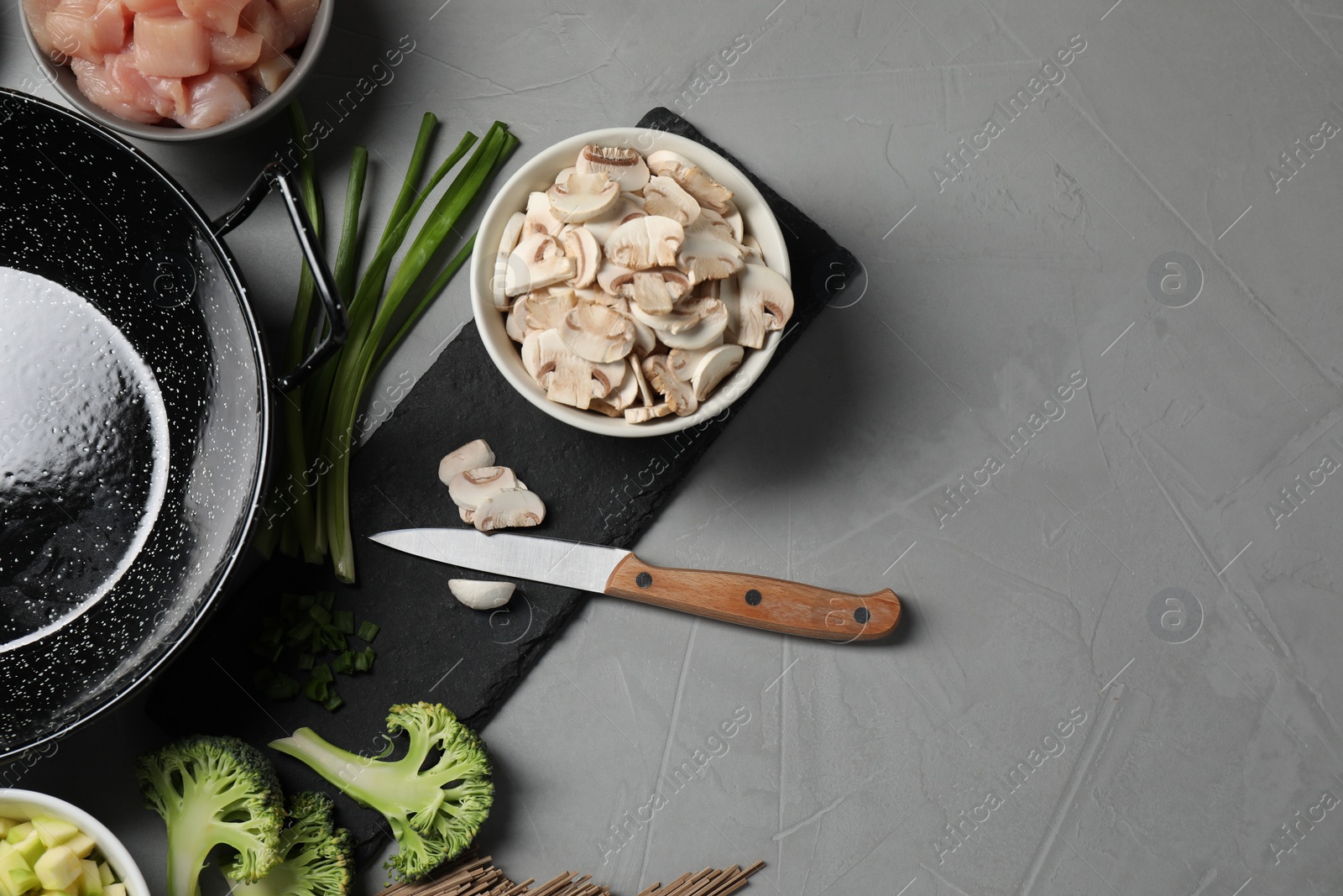 Photo of Wok pan, chicken and other products on light grey table, flat lay. Space for text