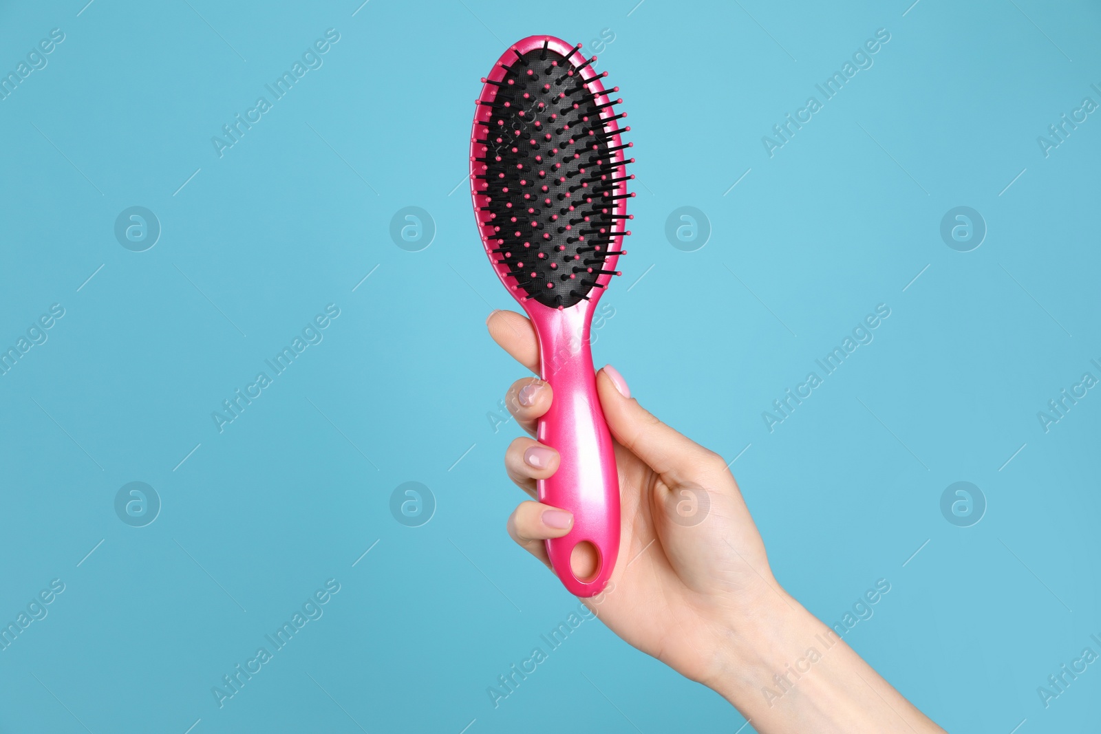 Photo of Woman holding hair brush against blue background, closeup. Space for text