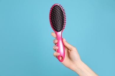 Woman holding hair brush against blue background, closeup. Space for text