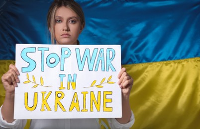 Photo of Sad woman holding poster with words Stop War in Ukraine near national flag. Space for text