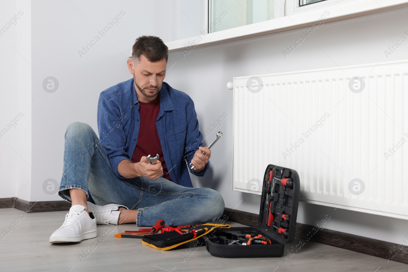 Photo of Man choosing wrench near box with tools indoors