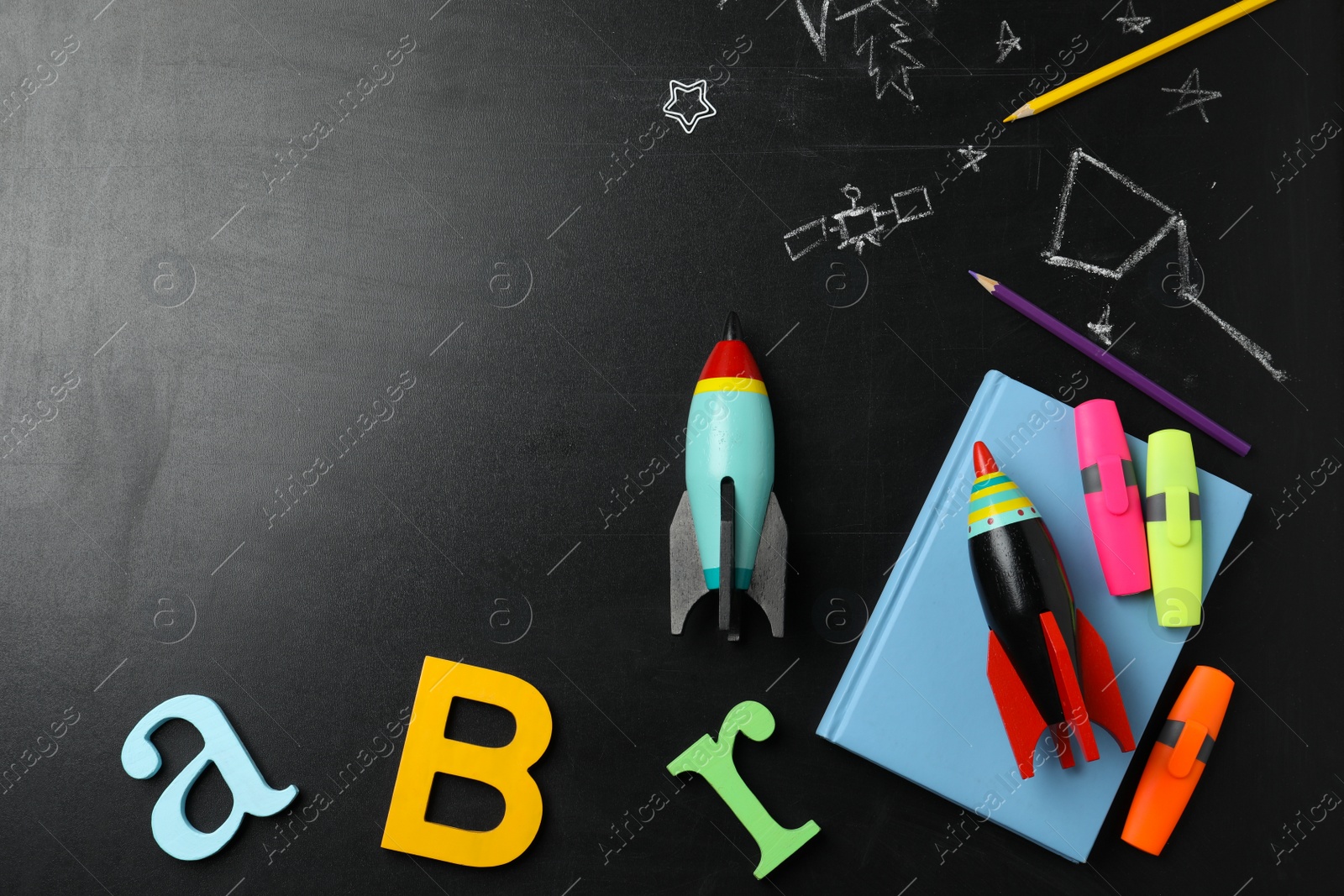 Photo of Bright toy rockets, school supplies and drawings on chalkboard, flat lay. Space for text