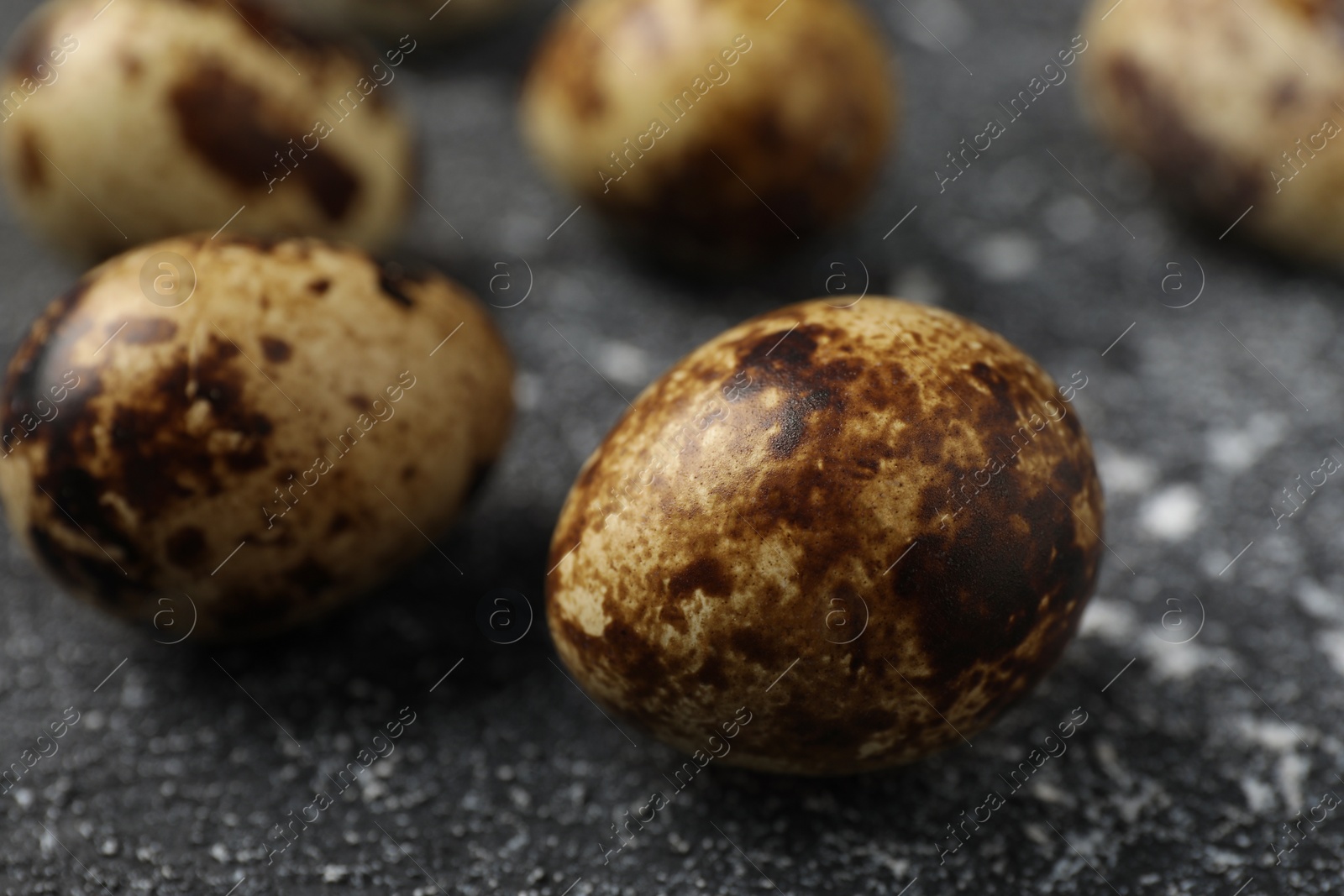 Photo of Many speckled quail eggs on black textured table, closeup