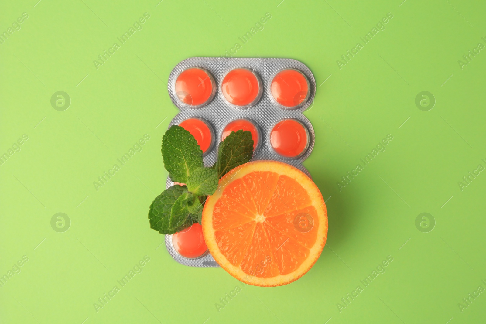 Photo of Fresh orange, mint leaves and blister with cough drops on light green background, flat lay