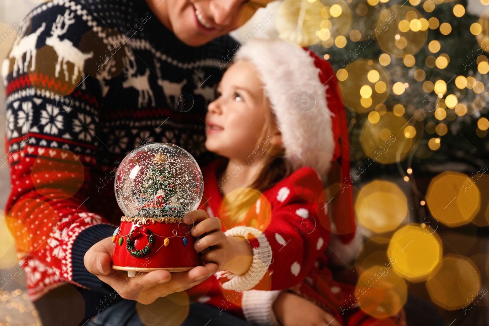 Image of Father and daughter with snow globe near Christmas tree, focus on toy. Bokeh effect