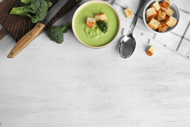 Photo of Delicious broccoli cream soup with croutons served on white wooden table, flat lay. Space for text