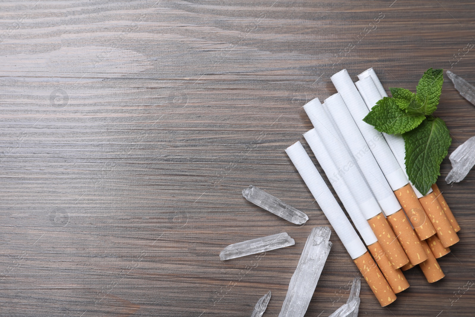 Photo of Cigarettes, menthol crystals and mint on wooden table, flat lay. Space for text