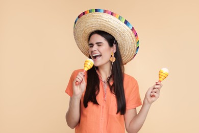 Photo of Young woman in Mexican sombrero hat with maracas on beige background