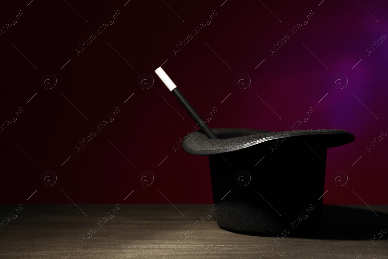 Photo of Magician's hat and wand on black wooden table against dark background, space for text