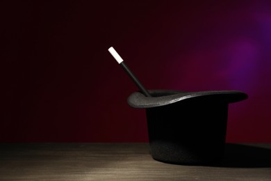 Photo of Magician's hat and wand on black wooden table against dark background, space for text