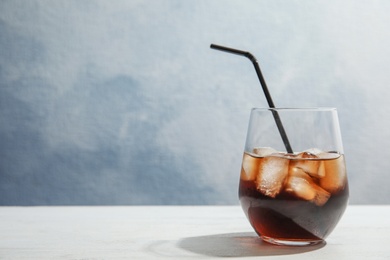 Photo of Glass of refreshing cola with ice cubes and straw on table. Space for text