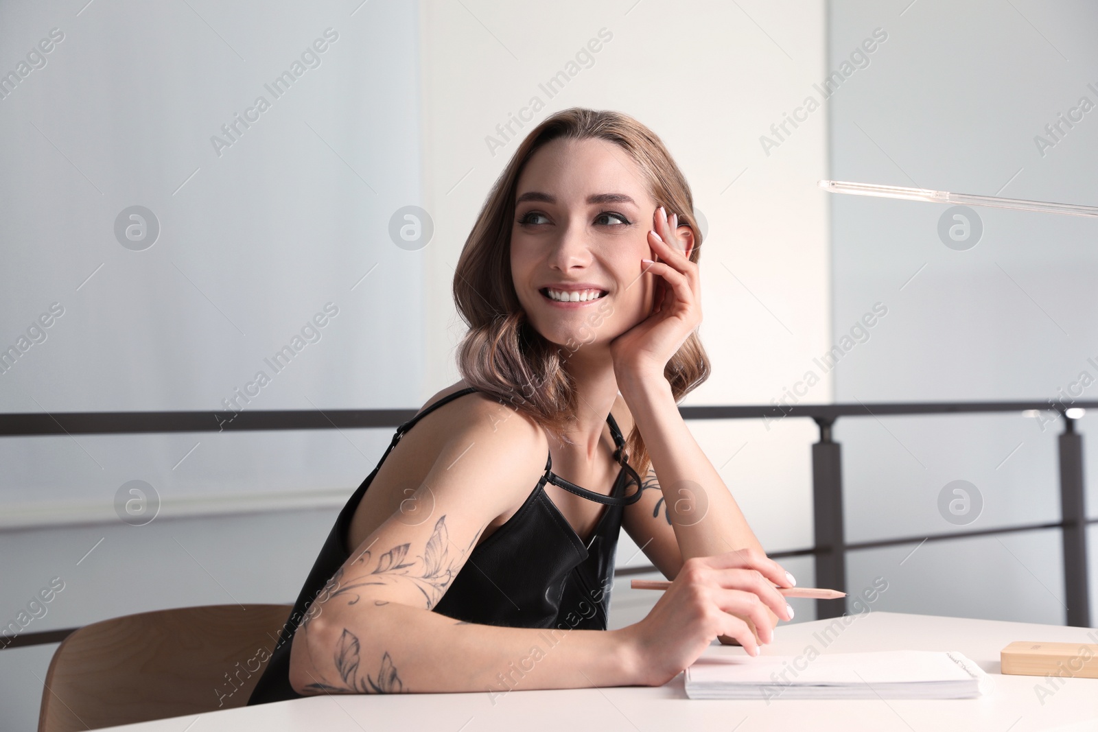 Photo of Beautiful woman with tattoos on body drawing in sketchbook at table indoors
