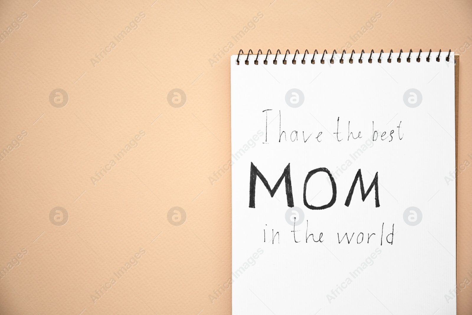 Photo of Notebook with text "I have the best mom in the world" on light background, top view. Mother's Day congratulation