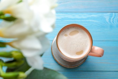 Mug of coffee and stylish cup coaster on turquoise wooden table, flat lay