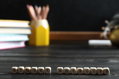 Photo of Cubes with phrase Winter Holidays on black wooden table in classroom. Space for text