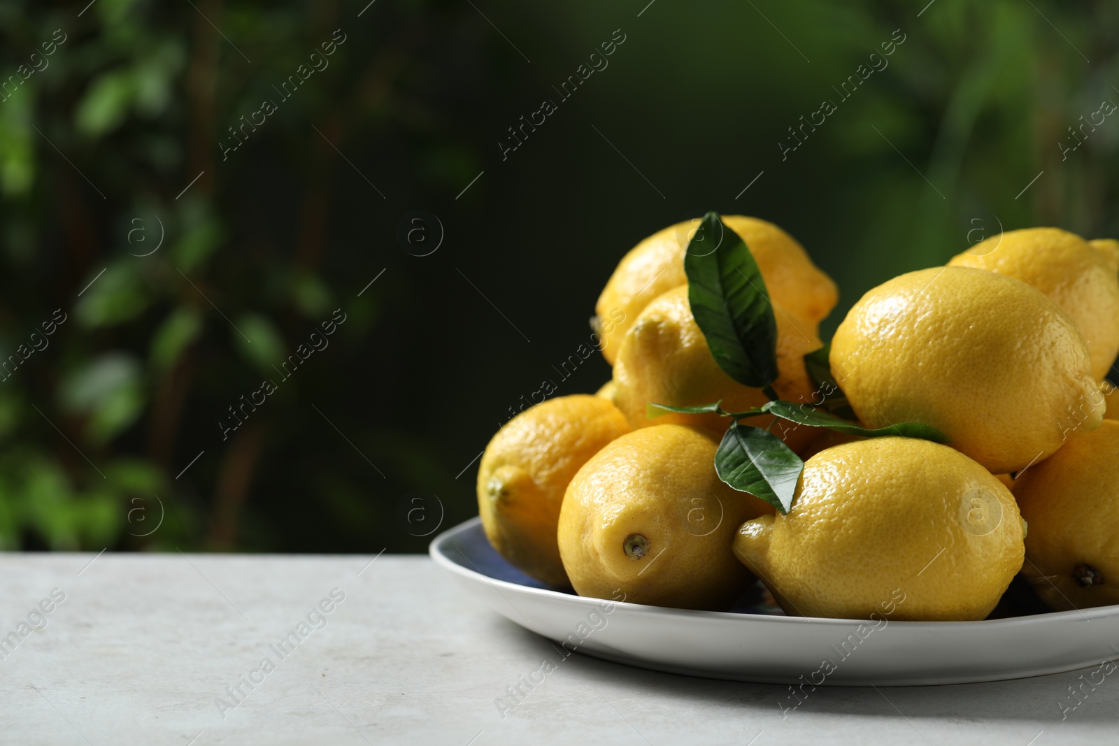 Photo of Fresh lemons and green leaves on table outdoors. Space for text