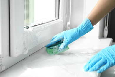 Woman cleaning window sill with sponge, closeup