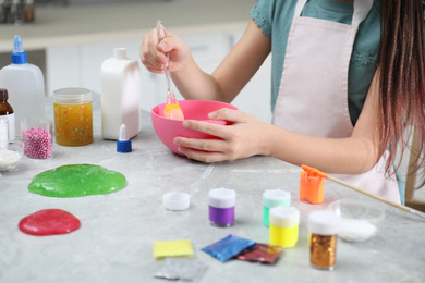 Photo of Little girl mixing ingredients with silicone spatula at table in kitchen, closeup. DIY slime toy