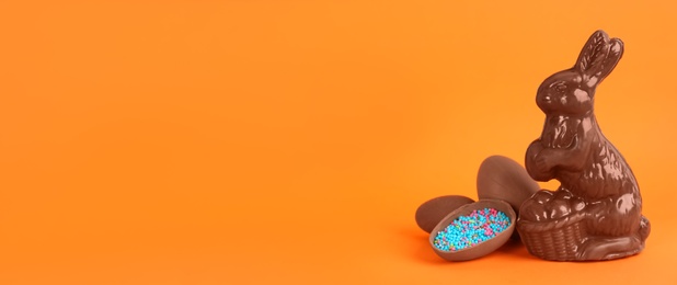 Photo of Chocolate Easter bunny and eggs on orange background. Space for text