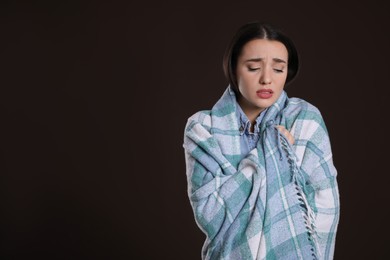 Photo of Young woman wrapped in blanket suffering from fever on dark background, space for text. Cold symptoms