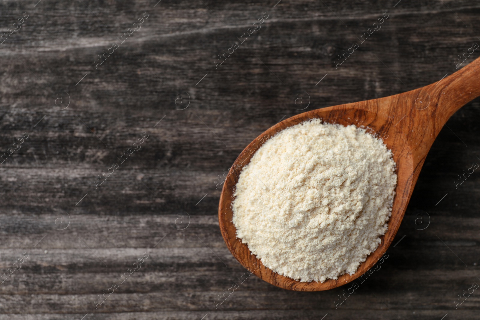 Photo of Spoon with quinoa flour on black wooden table, top view. Space for text