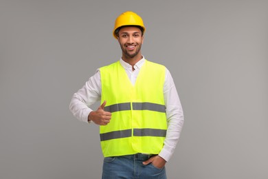 Engineer in hard hat showing thumb up on grey background