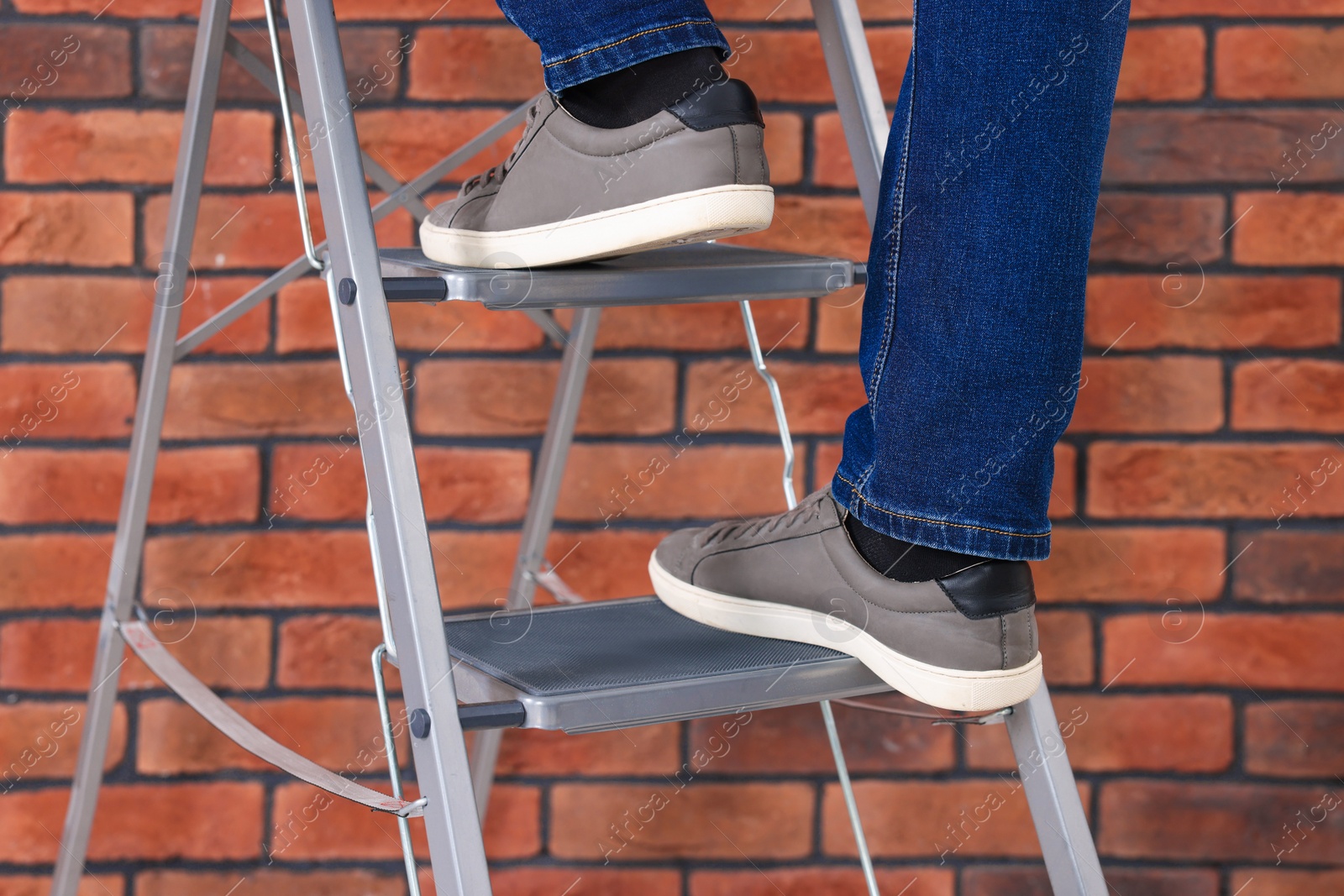 Photo of Man climbing up metal stepladder near brick wall, closeup