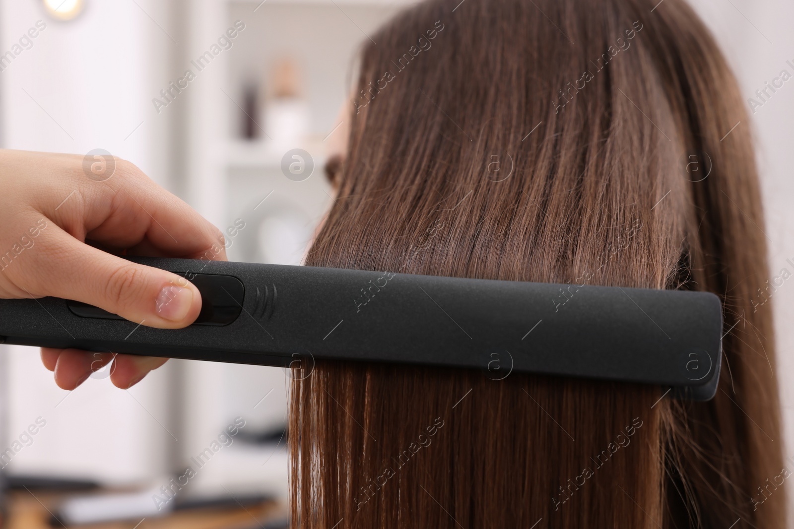 Photo of Hairdresser straightening woman's hair with flat iron in salon, closeup