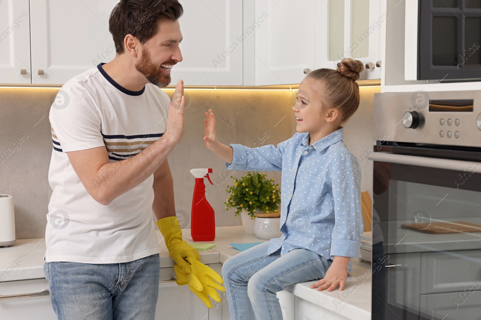 Photo of Spring cleaning. Father and daughter giving high five in kitchen